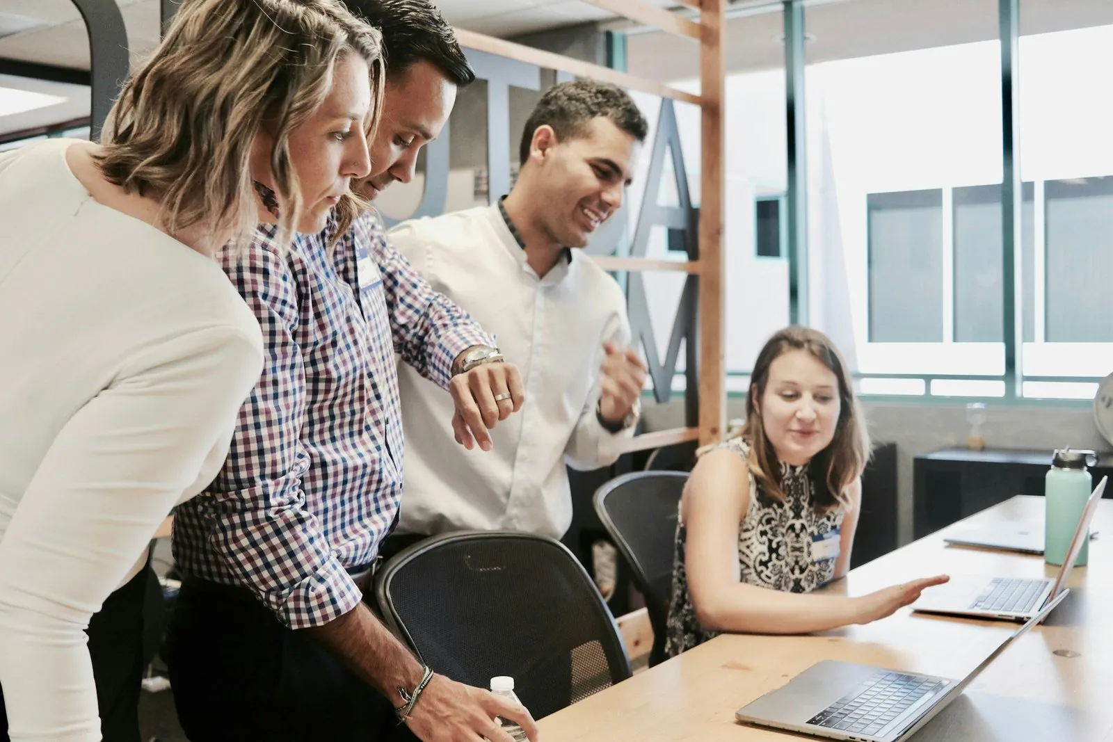 Four colleagues gathered around a laptop reviewing a website together